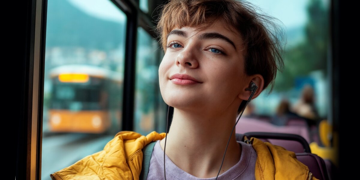 Słuchawki douszne HAMA Noble Czarny Młoda kobieta w żółtej kurtce używa czarnych słuchawek dousznych Hama podczas jazdy autobusem.