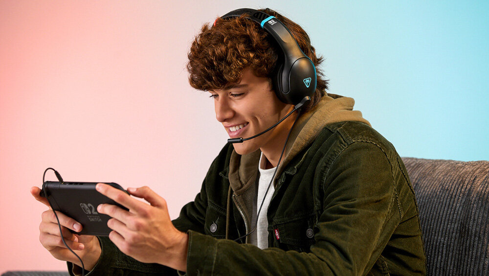 Słuchawki TURTLE BEACH Airlite Fit Nintendo Switch 2 gaming komfort dźwięk, osoba siedząca na fotelu z załozonymi słuchawkami trzymająca nintendo w rękach