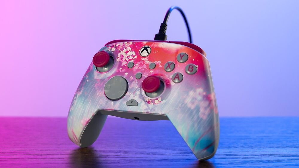 Kontroler TURTLE BEACH Xbox Rematch Advanced Kyoto Bloom TBC-2404-45 Frontowy widok pada Kyoto Bloom na ciemnym blacie, oświetlony nastrojowym fioletowo-różowym światłem nawiązanie do kraju Kwitnącej Wiśni warstwowe efekty wizualne wykończenie soczewkowe
