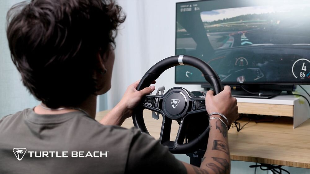 Kierownica Turtle Beach Velocity OneRace KD3 Widok zza pleców gracza na ekran monitora z grą wyścigową, dłonie spoczywają na kierownicy z logo Turtle Beach w rogu zdjęcia