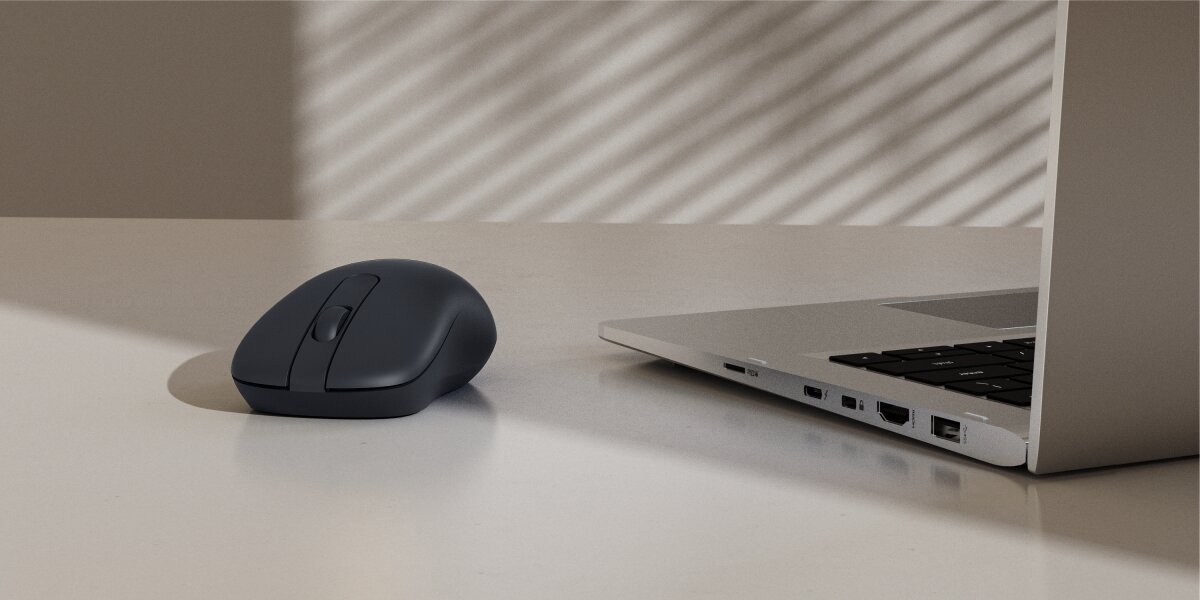 Czarna, bezprzewodowa mysz komputerowa o tradycyjnym kształcie, leżąca na biurku obok otwartego laptopa.