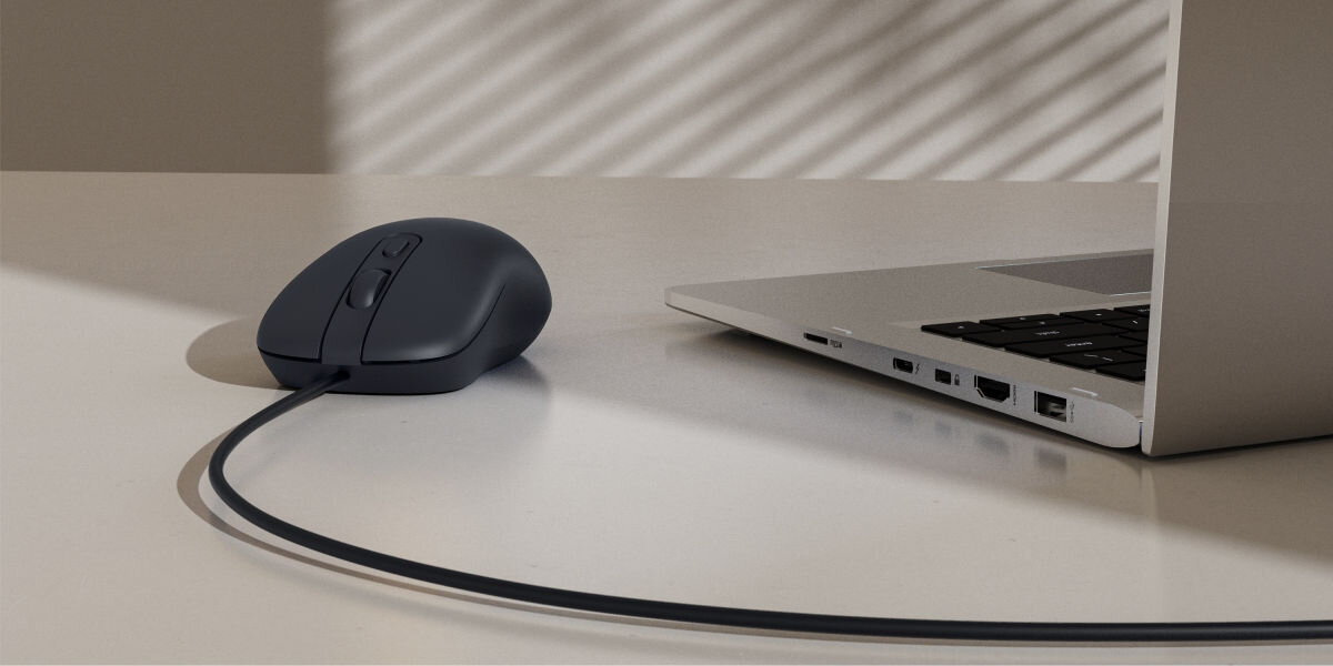 Precyzja i wygoda pracy Czarna, przewodowa mysz optyczna podłączona do laptopa leżącego na biurku, w otoczeniu naturalnego światła, ilustrująca jej użytkowanie w pracy biurowej.