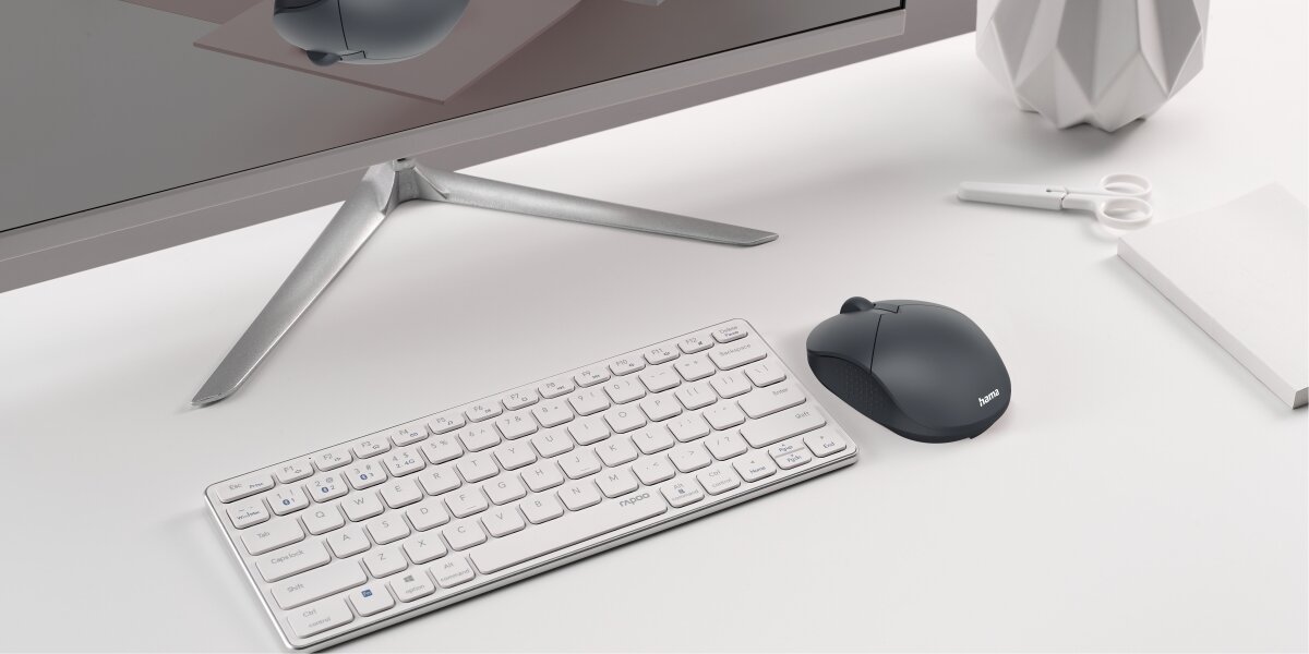 Ciemnoszara mysz Hama obok białej klawiatury bezprzewodowej na stanowisku pracy.