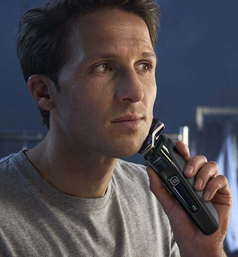 Osoba używa czarnej golarki elektrycznej z widocznym logo Philips. Golarka ma nowoczesny design z wyświetlaczem LED.