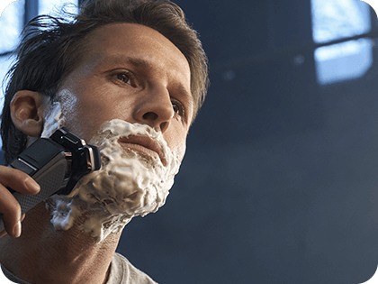 Osoba używa golarki elektrycznej do golenia twarzy pokrytej pianką do golenia.