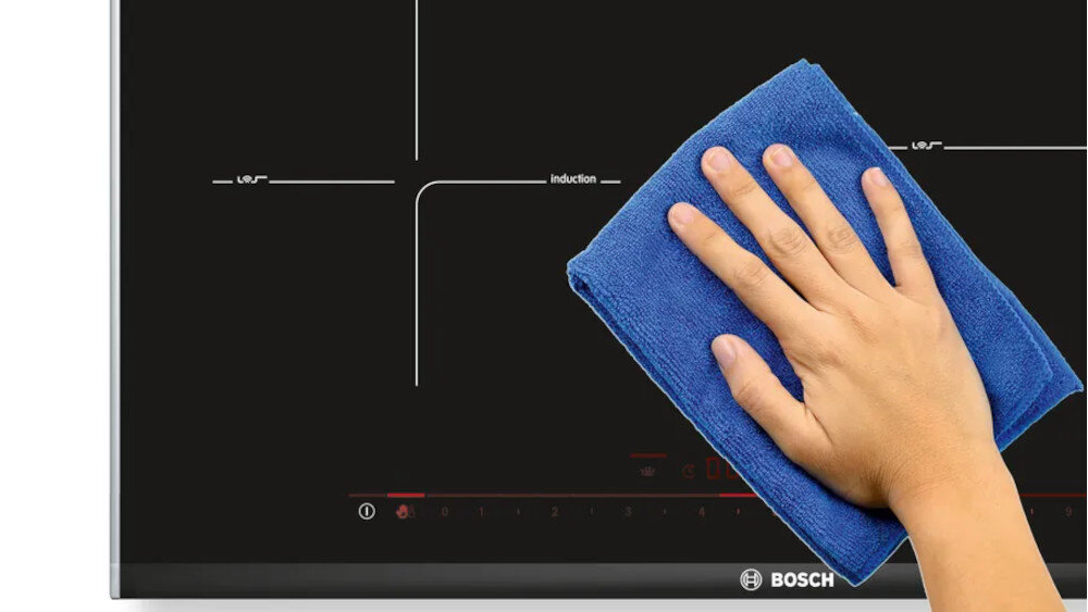 PŁYTA BOSCH PXL811H26E Funkcja Pauzy Na zdjęciu widoczna jest płyta indukcyjna Bosch, którą ktoś przeciera niebieską ściereczką z mikrofibry. Gładka, szklana powierzchnia i brak wystających elementów podkreślają łatwość czyszczenia urządzenia wstrzymanie nagrzewania blokada przycisków bezpieczeństwo wygoda łatwe czyszczenie