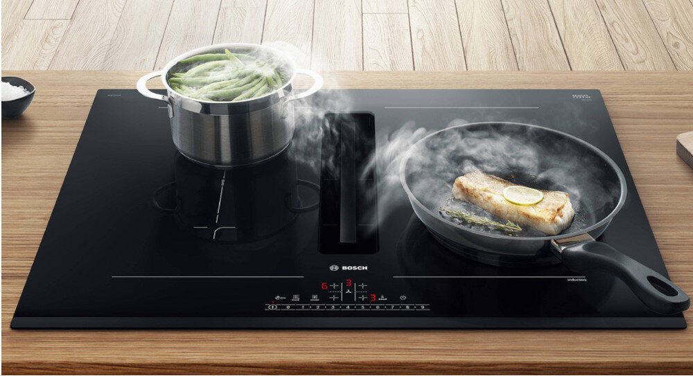 PŁYTA BOSCH PXL811H26E Na zdjęciu widoczna jest czarna płyta indukcyjna Bosch zintegrowana z wyciągiem środkowym, na której jednocześnie gotują się zielona fasolka w garnku i ryba na patelni. Para z naczyń jest zasysana bezpośrednio do wbudowanego wyciągu, co podkreśla wygodę gotowania na otwartej przestrzeni kuchennej Inteligentna wentylacja AutoOn automatyczne uruchamianie wentylacji świeże powietrze wygoda inteligencja komfort czystość świeżość