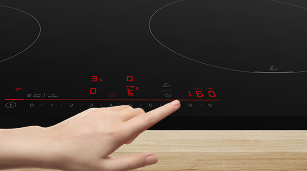 PŁYTA BOSCH PXL811H26E Na zdjęciu widać fragment czarnej płyty indukcyjnej z czerwonym, dotykowym panelem sterowania w dolnej części. Dłoń osoby obsługującej płytę wybiera poziom mocy, korzystając z podświetlonej skali numerycznej czujnik PerfectFry Plus monitorowanie wyświetlanie Temperatury ochrona przed przypaleniem 11 poziomów mocy Bez przypalenia