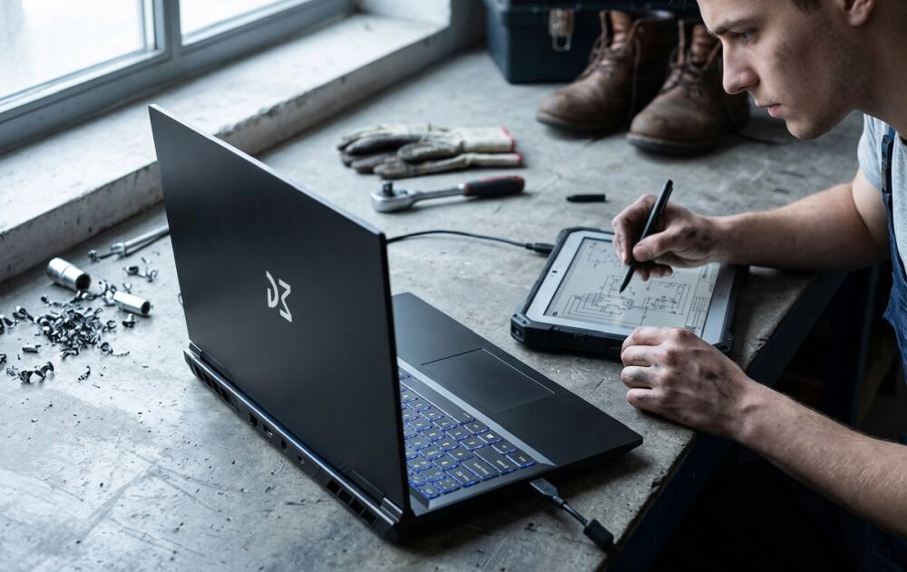 Osoba projektuje schemat techniczny obok laptopa Dream Machines z podświetlaną klawiaturą podczas pracy warsztatowej