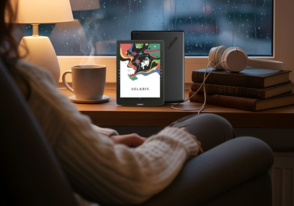 Czytnik e-booków INKBOOK Solaris Color 6 cali, Podświetlany ekran, Wi-Fi Czarny prezentacja czytnika w pokoju na parapecie obok książki kubek lampka przed kobieta siedząca na fotelu