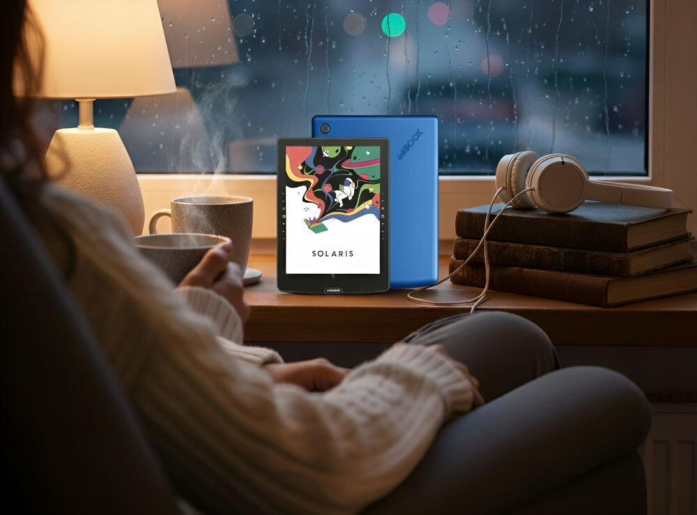 Czytnik e-booków INKBOOK Solaris Color 6 cali, Podświetlany ekran, Wi-Fi Niebieski prezentacja czytnika w pokoju na parapecie obok książki kubek lampka przed kobieta siedząca na fotelu