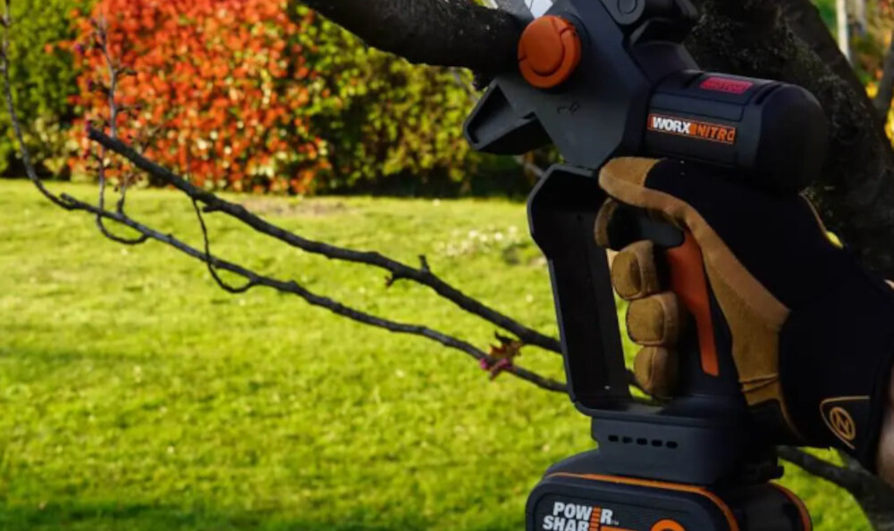 Piła akumulatorowa WORX Nitro WG325E ogród osoba przycina gałąź na drzewie zbliżenie na rękojeść ergonomiczny uchwyt górna osłona chroniąca dłoń wpływa na pewność chwytu do obsługi jedną ręką blokada bezpieczeństwa automatyczny hamulec bezpieczeństwa w codziennych pracach