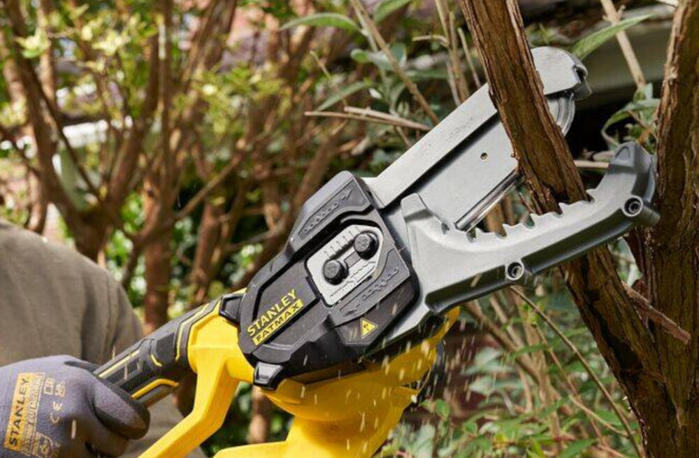 Sekator do gałęzi akumulatorowy STANLEY SFMCPS515M1-QW zbliżenie na ostrza osoba przycina gałęzie opatentowana konstrukcja szczęk skutecznie zaciska gałęzie zwiększając kontrolę nad cięciem minimalizując ryzyko poślizgu całkowicie zamknięta prowadnica i łańcuch chronią dłonie i ciało bezpieczeństwo pracy