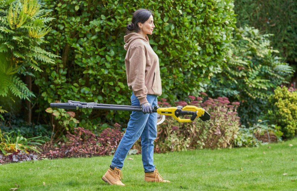 Sekator do gałęzi akumulatorowy STANLEY FatMax SFMCPP632B-XJ ogród osoba idzie po trawniku w dłoni trzyma złożony sekator w tle krzewy drzewa cięcie bez wysiłku zadbany ogród uniwersalność skuteczność