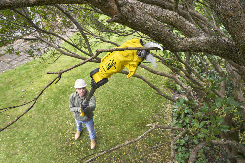 Sekator do gałęzi akumulatorowy STANLEY FatMax SFMCPP632B-XJ ogród osoba stoi na trawniku w dłoni trzyma sekator tnie gałęzie w koronie drzewa widok z góry składany system tyczki o długości do 2,4 m bezpieczne sięganie do wysokich gałęzi bez potrzeby korzystania z drabiny można pracować z ziemi bezpieczeństwo i komfort wysięgnik można złożyć