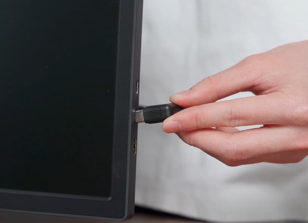 Monitor EXTRALINK Smart Life S3 Zbliżenie na rękę wkładającą przewód USB-C do portu bocznego monitora, podłączenie, porty, gniazda