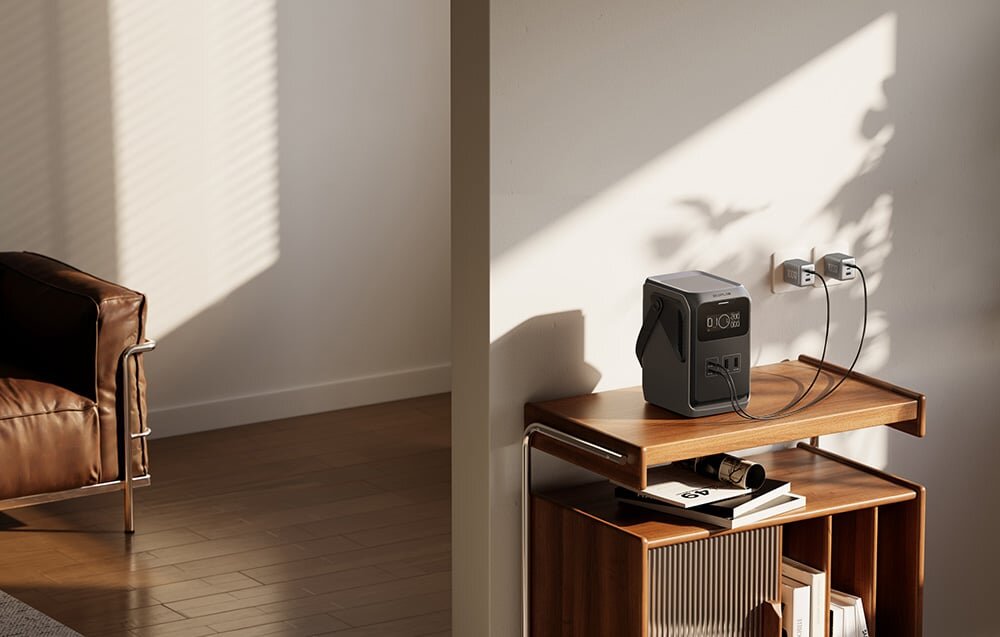 Stacja zasilania ECOFLOW Trail 200 DC, bateria, LFP, cykle, outdoor, EcoFlow River 2 Pro na plaży: stacja z wyświetlaczem 50%, portami USB i AC ładuje głośnik Bluetooth oraz iPhone'a na stoliku kempingowym.