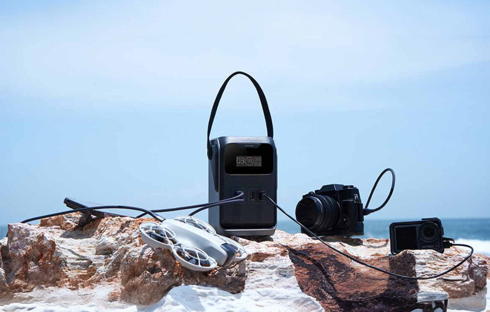 Stacja zasilania ECOFLOW Trail 200 DC, X-Guard, przepięcie, zwarcie, temperatura, Kobieta w turbanie trzyma EcoFlow River 2 Pro z wyświetlaczem 90% i portami na rowerze kempingowym przy jeziorze.