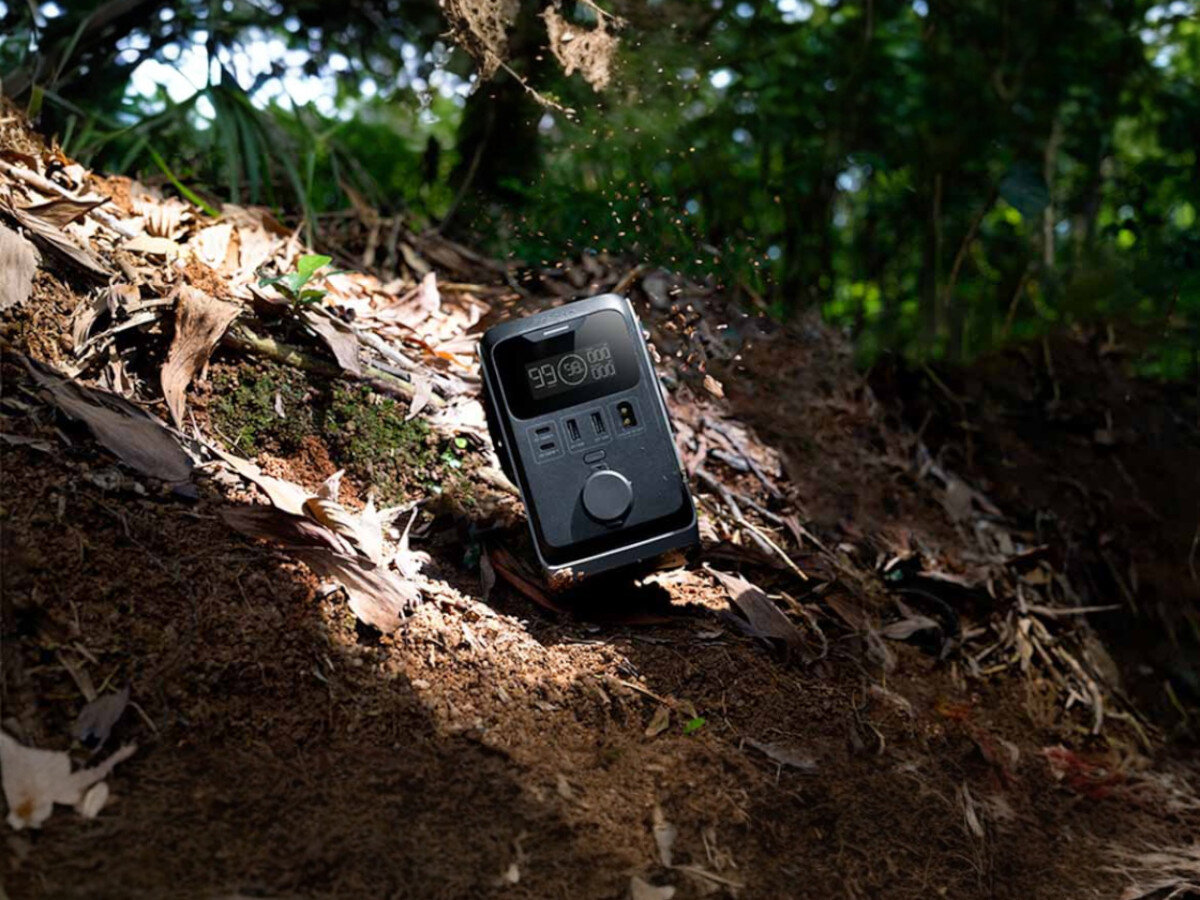 Stacja zasilania ECOFLOW Trail 300 DC, X-Guard, przepięcie, zwarcie, temperatura, Kobieta w turbanie trzyma EcoFlow River 2 Pro z wyświetlaczem 90% i portami na rowerze kempingowym przy jeziorze.