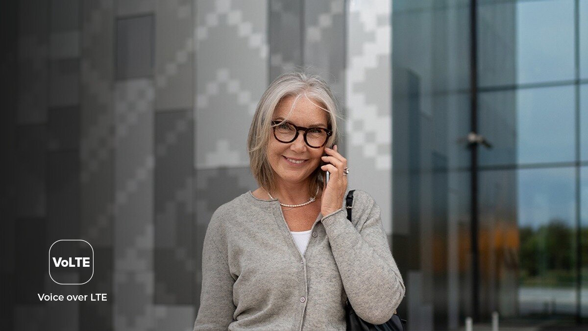 Zdjęcie lifestyle do myPhone 3510 LTE - kobieta w okularach rozmawia przez telefon przed nowoczesnym, szklanym budynkiem; ikona VoLTE.