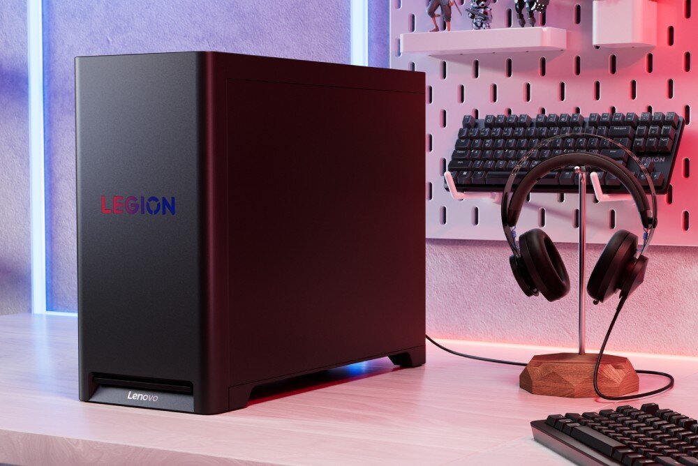 Komputer LENOVO Legion T5 30AGB10 Komputer ustawiony na biurku, widok od boku na czarną obudowę z logo 'LEGION', obok stojak ze słuchawkami i klawiatura na ścianie