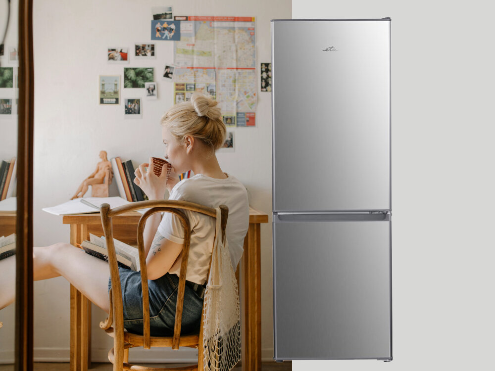 Lodówka ETA ETA385690010C Lodówka w stalowym wykończeniu ustawiona przy biurku, przy którym młoda kobieta pije napój w przytulnym, domowym wnętrzu szklane półki wysoka wytrzymałość przezroczyste szuflady półki drzwiowe dobra organizacja trwałość