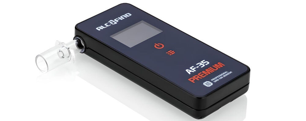 Na zdjęciu widoczny jest alkomat z napisem \'ALCOFIND\' oraz oznaczeniami \'AF-35 PREMIUM\'. Urządzenie ma ciemną obudowę i wyświetlacz, a z boku znajduje się ustnik.