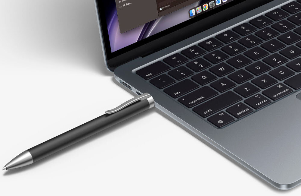 Laptop z otwartym ekranem i klawiaturą, do którego podłączony jest czarny długopis z metalowym klipsem. Na ekranie widoczny jest fragment interfejsu użytkownika.