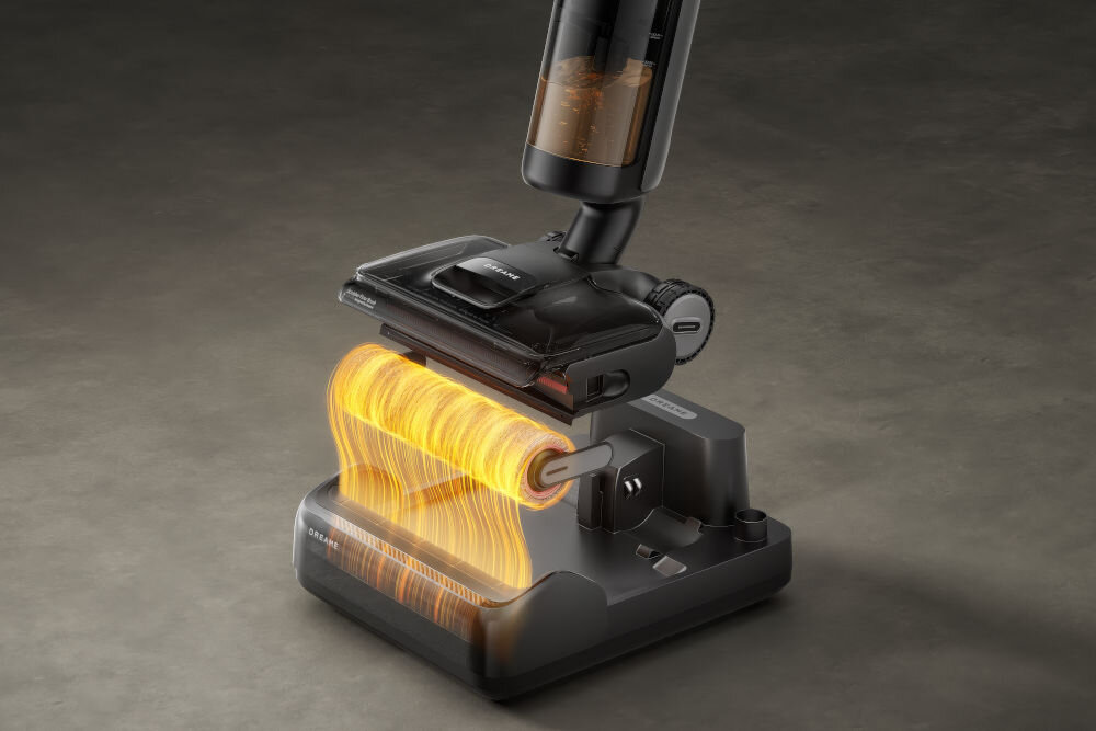 Na obrazie widoczny jest odkurzacz z przezroczystym pojemnikiem na kurz, umieszczony na stacji dokującej. Widać efekt wizualny przedstawiający przepływ powietrza przez szczotkę odkurzacza.