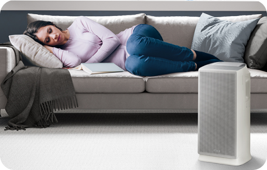 Osoba leżąca na sofie z oczyszczaczem powietrza w tle, w spokojnym otoczeniu.