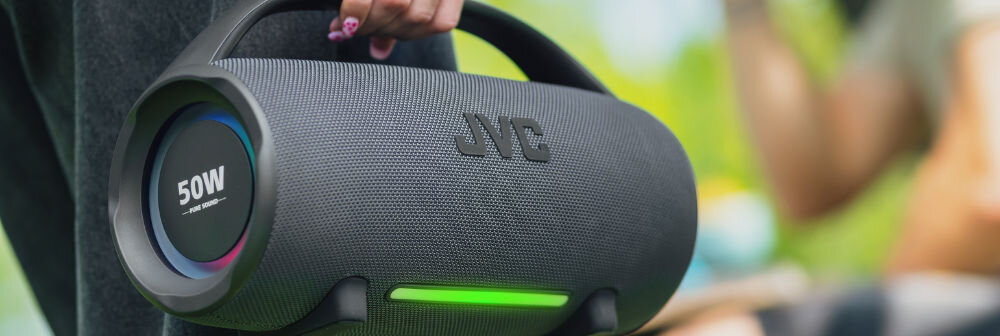 Głośnik mobilny JVC XS-E524B obudowa cylindryczna radiatory pasywne uchwyt, osoba trzymająca głośnik za uchwyt