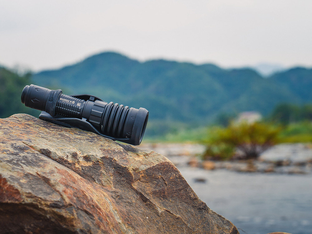 Latarka OLIGHT Warrior X4 Kit OL002925, LED, wibracje, niski stan, bateria, Warrior X4 w kaburze na skale nad rzeką