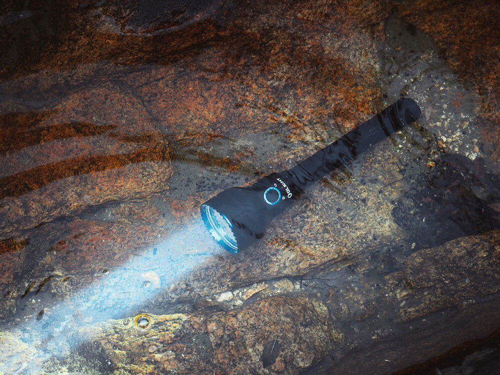 Latarka OLIGHT Javelot Turbo 2 OL003991 Czarny, akumulatory, tryby, USB-C, magnetyczne, Olight Javelot Turbo 2 Black świeci pod wodą, wytrzymałość IP67, latarka w kamienistym strumieniu.