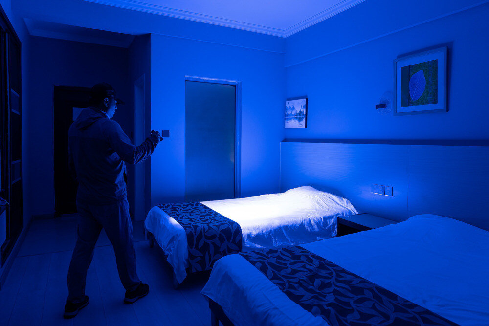 Latarka OLIGHT Arkfeld Ultra UV OL690971 Oliwkowo-szary, tryby, jasność, stroboskop, moonlight, Mężczyzna sprawdza łóżka niebieskim światłem