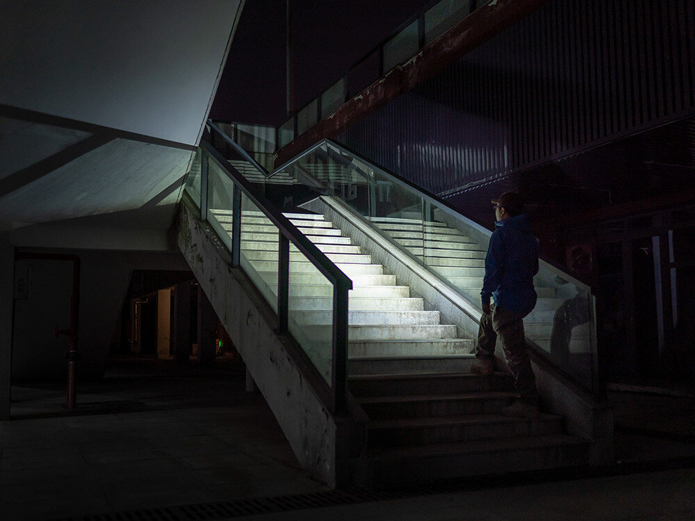 Latarka OLIGHT iMini 2 OL001652 Czarny, łatwość, intuicyjność, szybki start, jedna ręka, Olight oświetla klatkę schodową po zmroku, mężczyzna stoi na dole schodów na zewnątrz.