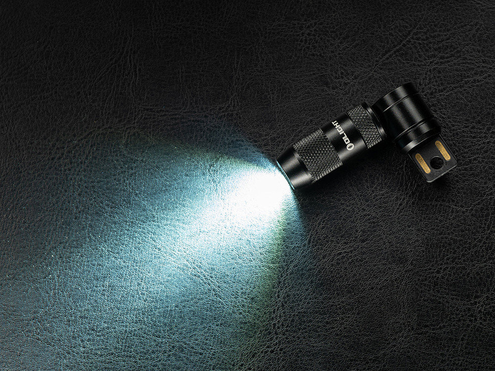 Latarka OLIGHT iMini 2 OL004417 Pomarańczowy, aluminium, trwałość, odporność, wodoodporność, Latarka Olight iMini 2 świeci szerokim białym strumieniem na czarną, skórzaną powierzchnię.