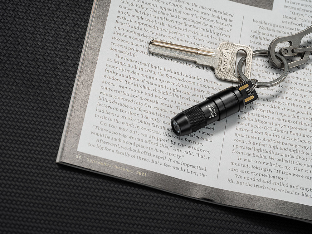 Latarka OLIGHT iMini 2 OL692265 Czerwony, światło, codzienność, klucze, szybkie użycie, Brelok Olight iMini 2 przypięty do kluczy, leży na otwartej książce, zdjęcie z góry.