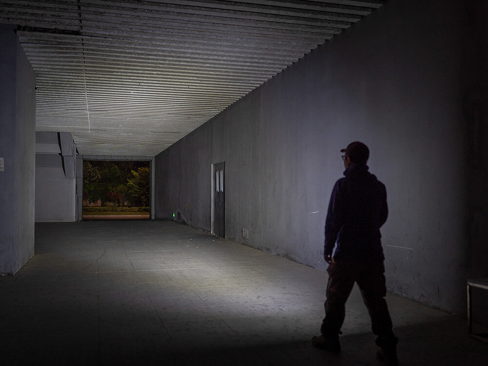 Latarka OLIGHT iMini 2 OL692265 Czerwony, USB, szybkie ładowanie, magnetyczna nasadka, wygoda, Mocna biała wiązka światła latarki Olight w ciemnym, pustym pomieszczeniu, sylwetka mężczyzny.