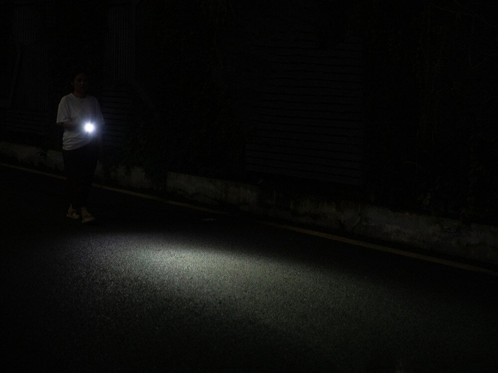 Latarka OLIGHT I3E EOS OL692340 Niebieski, światło, brelok, ergonomia, codzienny, Kobieta idzie nocą z latarką, strumień światła oświetla asfalt, ciemna ulica.