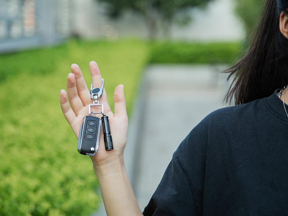 Latarka OLIGHT I3E EOS OL691510 Niebieski, aluminium, anodyzacja, IPX8, wytrzymałość,  Latarka Olight I3E EOS przy kluczach samochodowych, detal na tle zieleni, kobieca ręka.