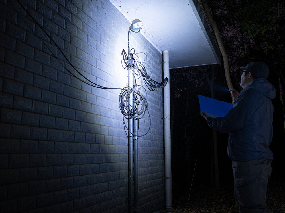 Latarka OLIGHT I1R II EOS Kit, brelok, latarka, ergonomia, światło, Mężczyzna oświetla instalację elektryczną przy budynku latarką Olight, prace nocą