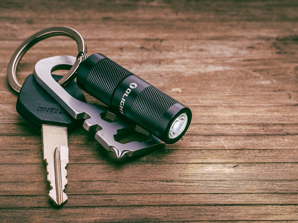 Latarka OLIGHT I1R II EOS Kit, mała, brelok, 150 lumenów, codzienny,  Latarka Olight I1R 2 EOS czarna, brelok przy kluczach i narzędziu, drewniane tło, EDC.