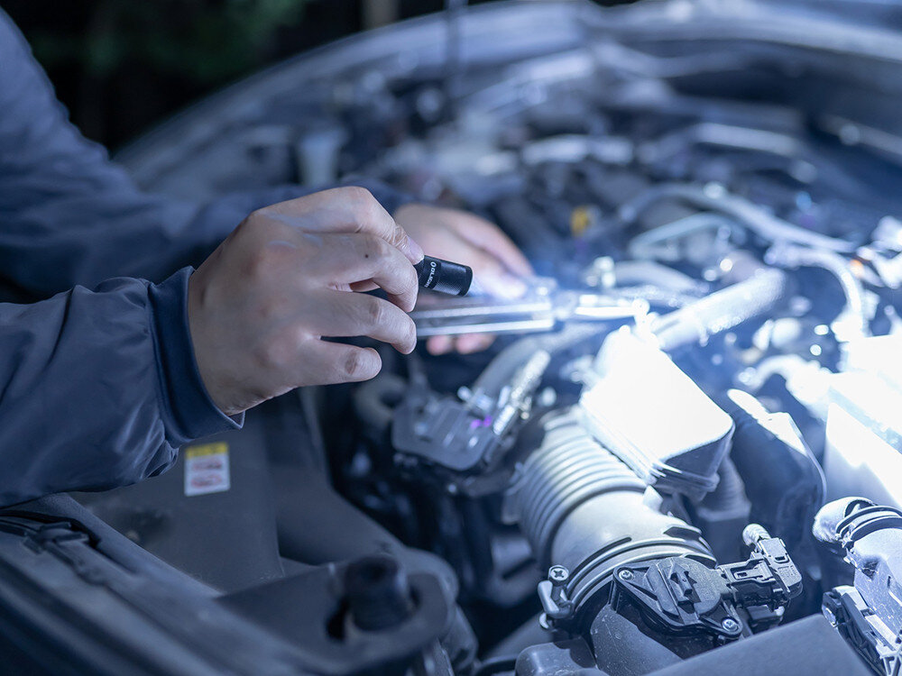 Latarka OLIGHT I1R II EOS Kit, 44 mm, 13 gramów, klucze, ergonomia, Latarka Olight oświetla komorę silnika auta podczas naprawy nocą, szczegół ręki.