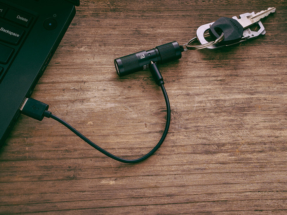 Latarka OLIGHT I1R II EOS Kit, Micro-USB, dioda, ładowanie, sygnalizacja, Czarna I1R 2 EOS ładowana przez kabel Micro-USB, kluczyki, laptop, drewniany blat.