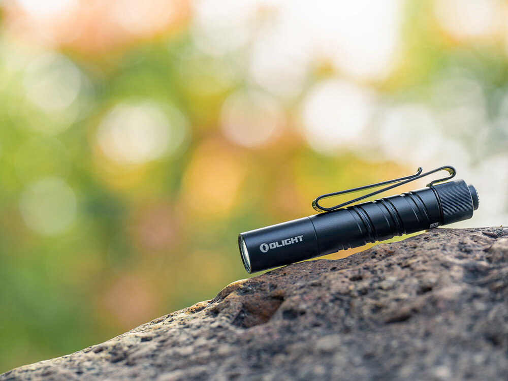 Latarka OLIGHT I3T 2 EOS OL002901 Czarny, mała latarka, ergonomiczne oświetlenie, EDC sprzęt, intensywny strumień, Latarka Olight I3T 2 EOS na skale, rozmyte kolorowe tło, kompaktowa latarka EDC