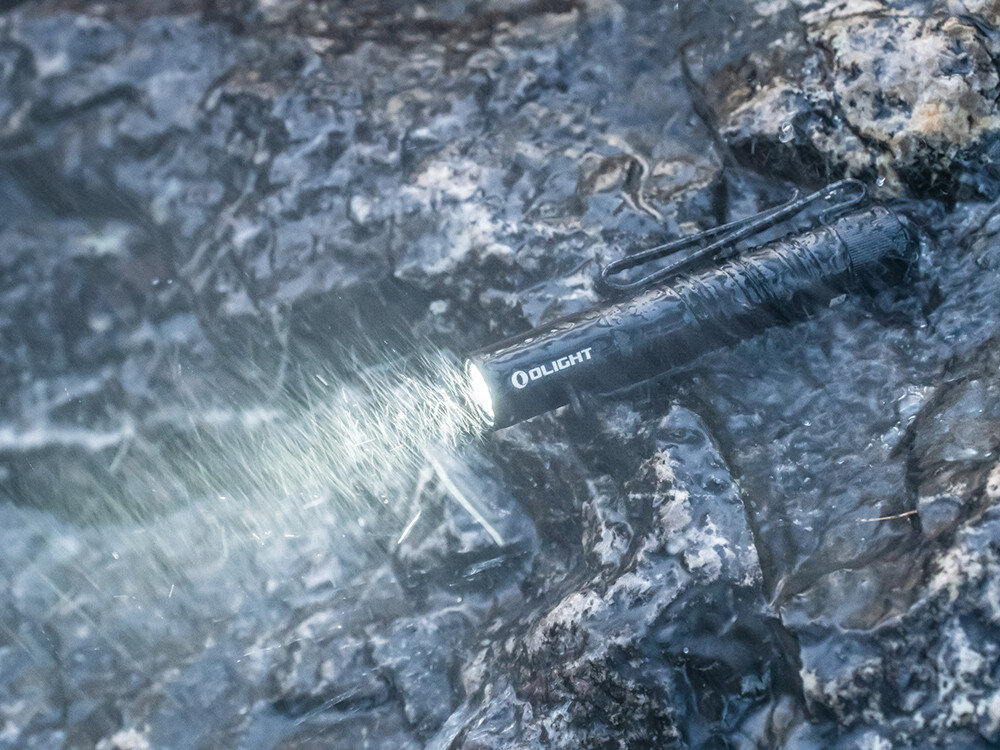Latarka OLIGHT I3T 2 EOS OL002901 Czarny, aluminiowy korpus, odporność na wodę, trwała obudowa, solidne wykonanie, Latarka Olight I3T 2 EOS świeci w ulewnym deszczu, mokre kamienie, podkreślona wodoodporność