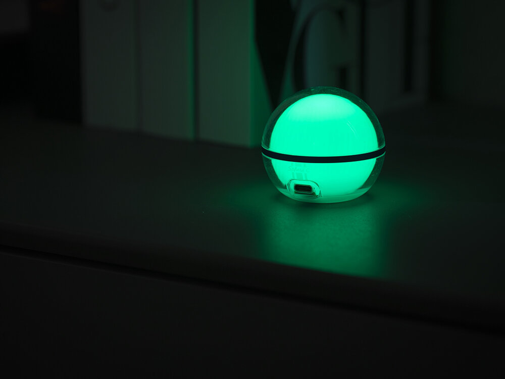 Lampa kempingowa OLIGHT Sphere C OL692302, światło, inteligentna kula, 75 lumenów, rozproszenie, Lampka Olight Sphere świeci na zielono, ustawiona na ciemnej półce.