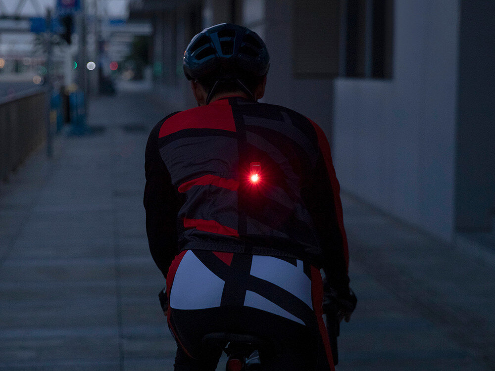 Latarka OLIGHT OL004547, floodlight, spotlight, czerwone, SOS, Oclip Pro zamontowana na plecach kolarza, tryb czerwony, podkreślenie widoczności na drodze.