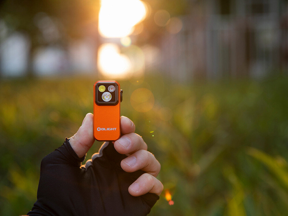 Latarka OLIGHT OL690834, szybkie ładowanie, USB-C, akumulator, gotowość, Oclip Pro trzymana w rękawiczce na tle zachodzącego słońca i zieleni, outdoor, wieczór.