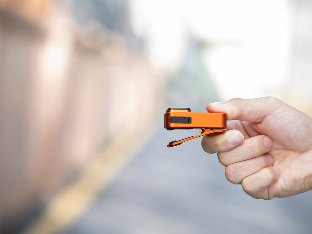 Latarka OLIGHT OL690834, magnes, klips, montaż, linka, Latarka Oclip Pro z klipsem w palcach, profil boczny, jasne rozmyte otoczenie, lekkość.